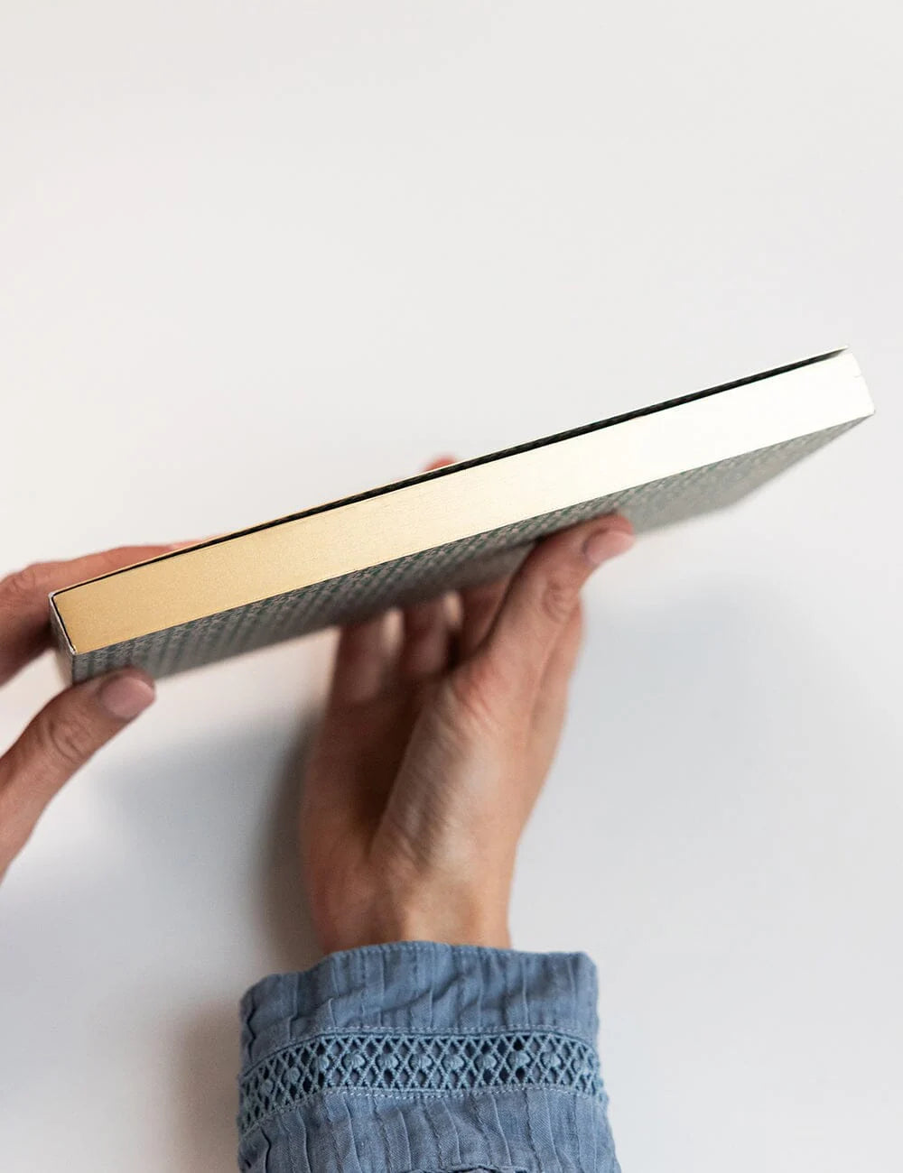 Person holding a rectangular object with gold and silver finishes on a white background