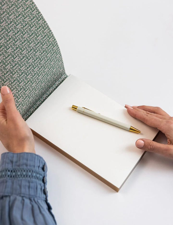 Person holding a pen over an open book on a white surface
