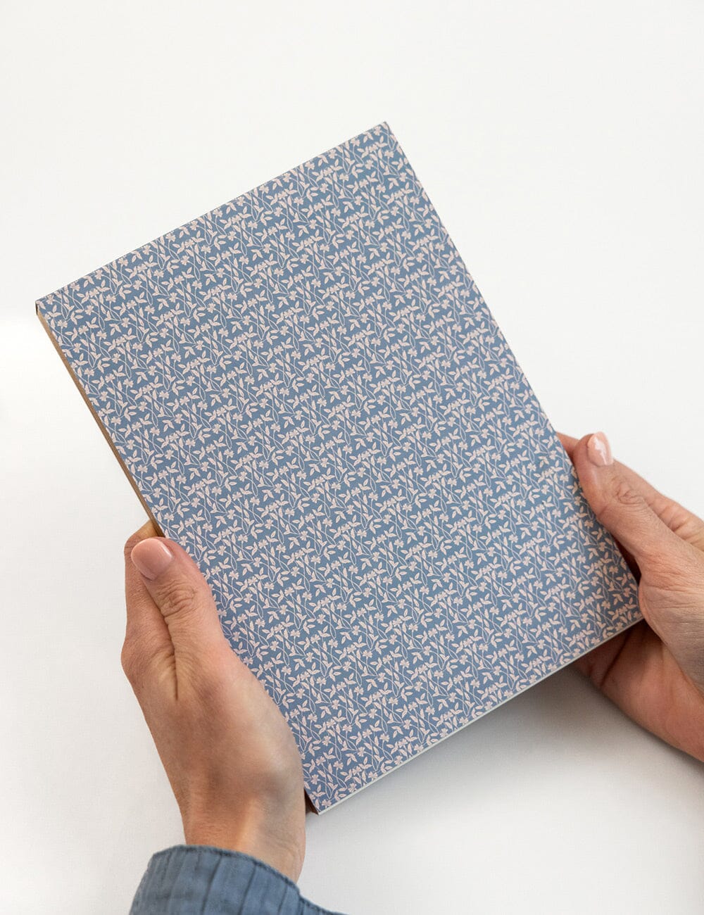 Person holding a blue patterned notebook on a white background