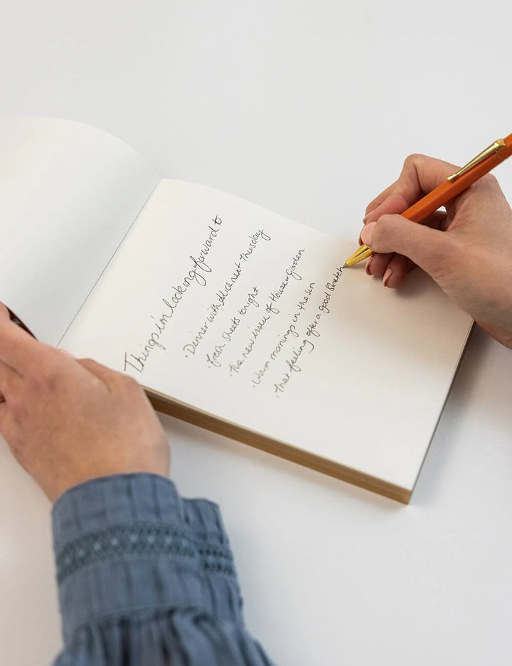 Person writing in a notebook with a pen on a white surface