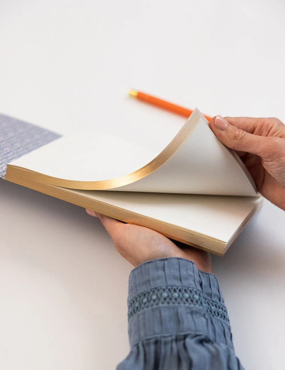 Person holding an open notebook with a pen on a light surface
