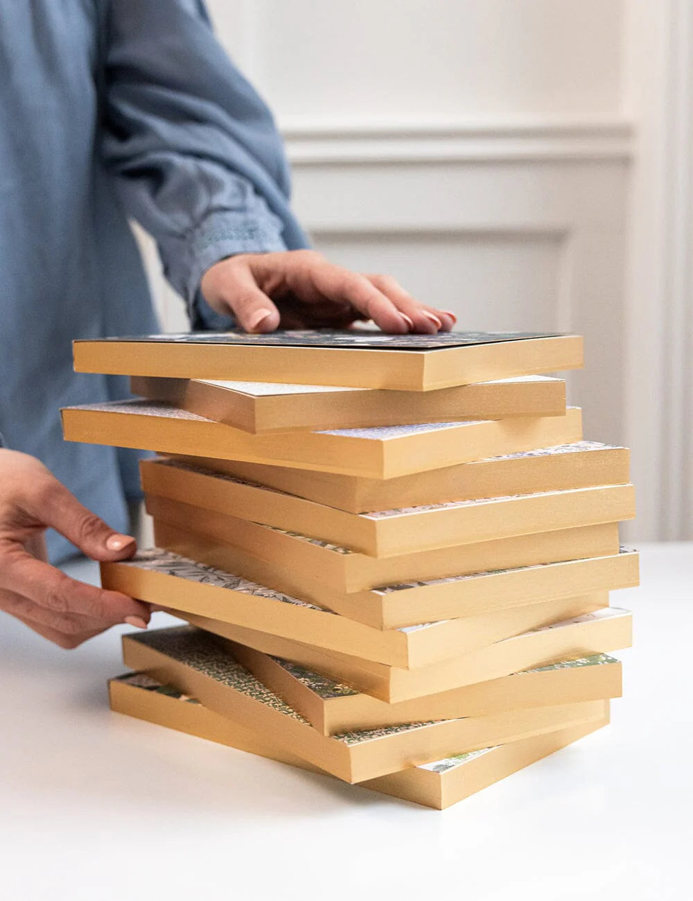 Stack of books with a person's hand reaching towards the top book on a light background