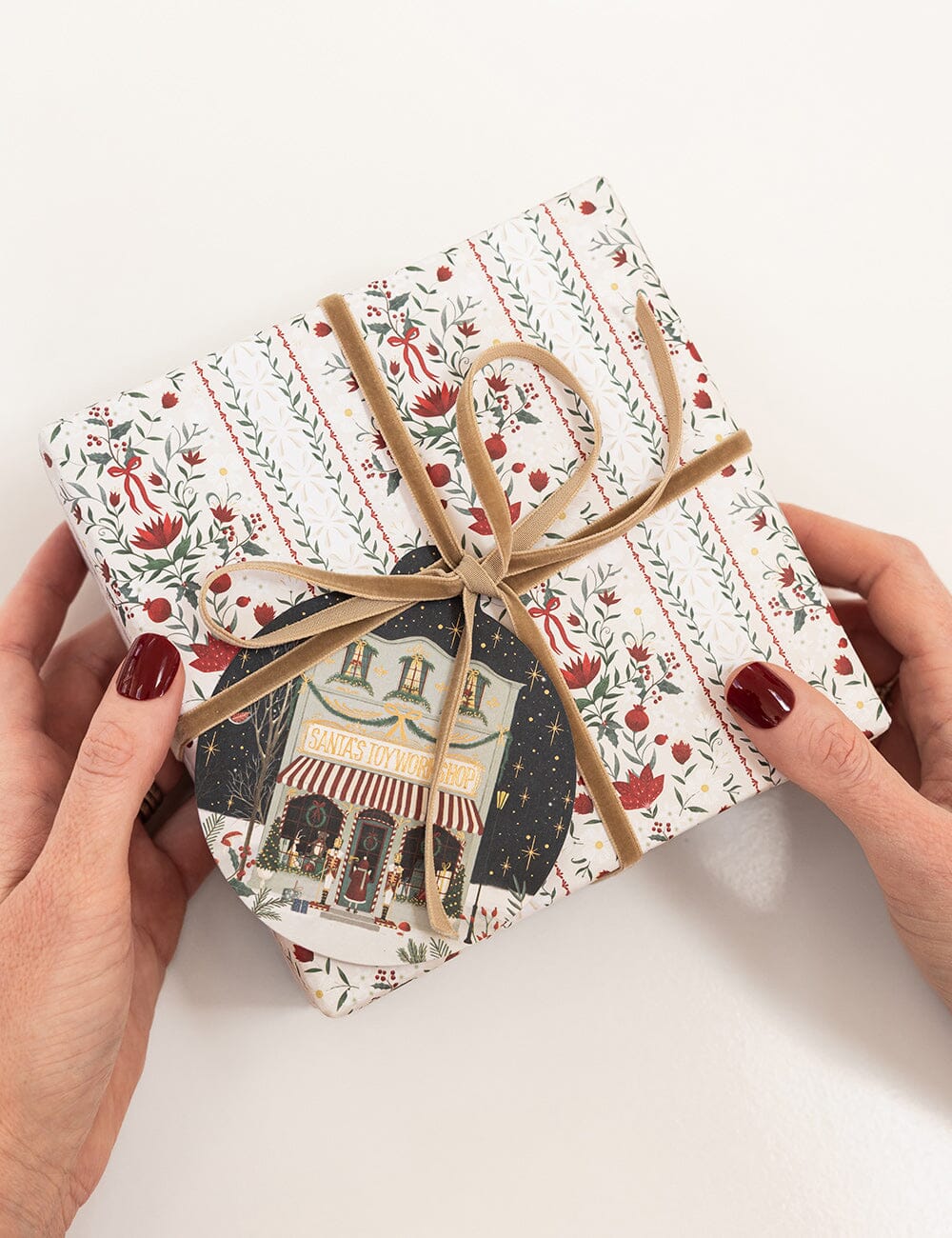 Gift box with decorative wrapping paper and ribbon, held by hands on a white background