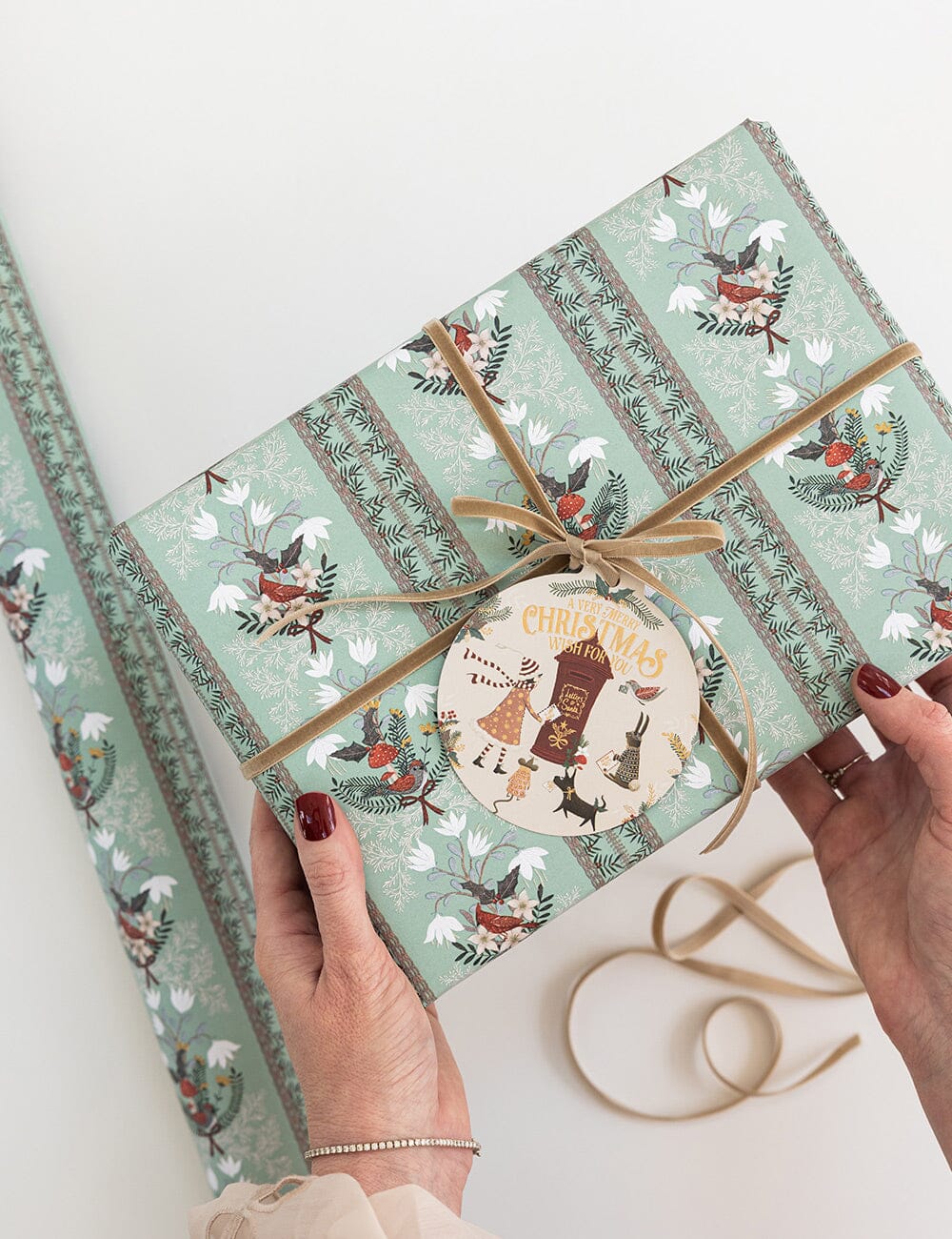Gift wrapped in festive paper with a decorative ribbon and label, held by hands on a light background.