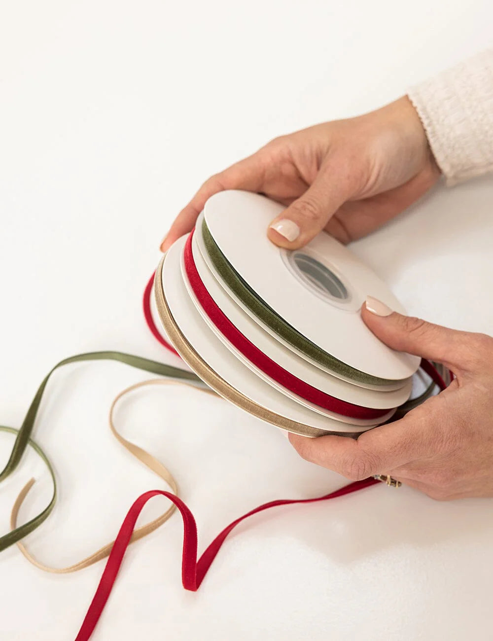 Person holding a spool of ribbon with red, green, and beige ribbons on a white background