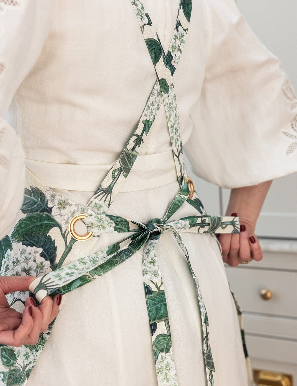 White dress with a green floral apron being adjusted by hands.