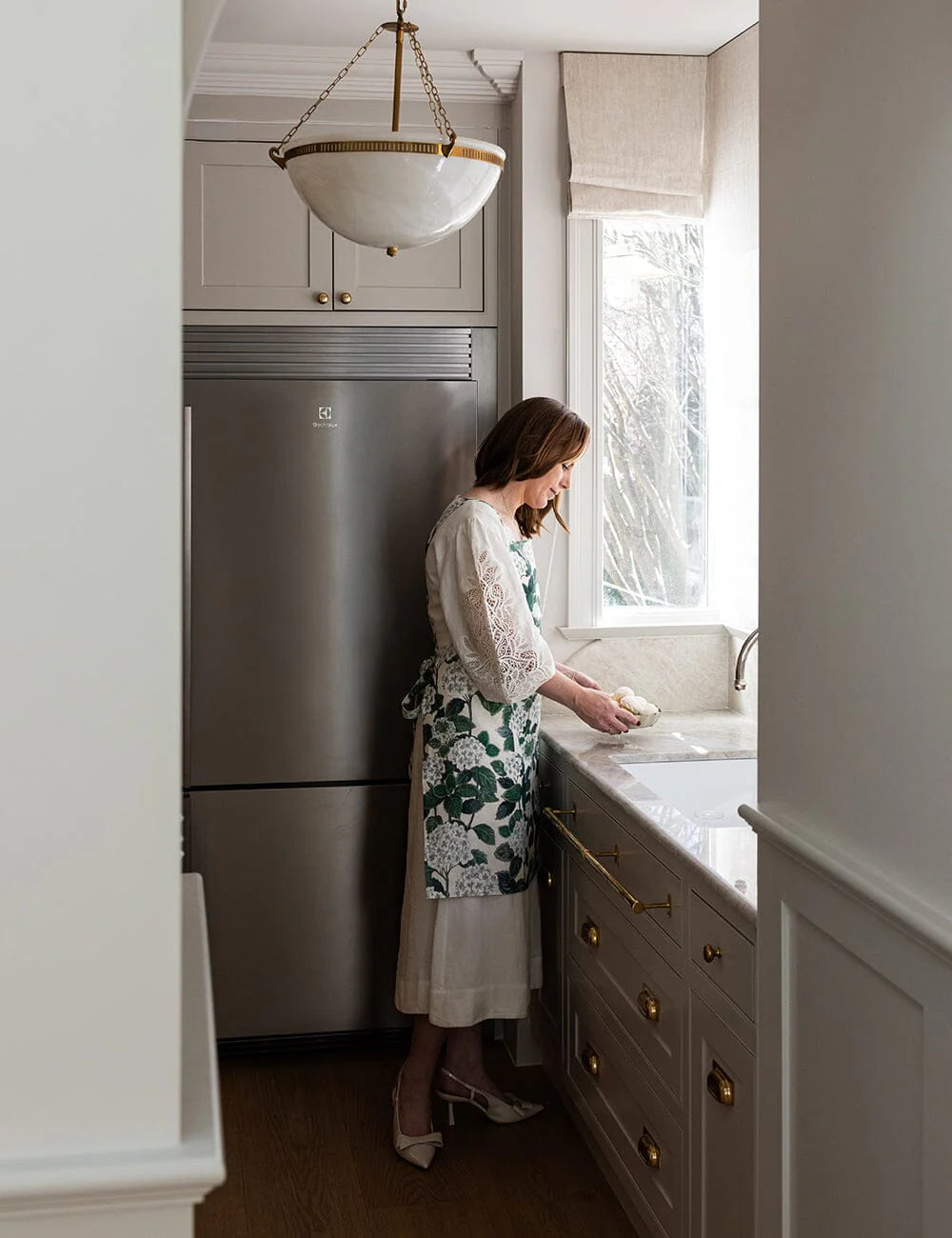 Woman in a kitchen washing dishes in a floral green apron