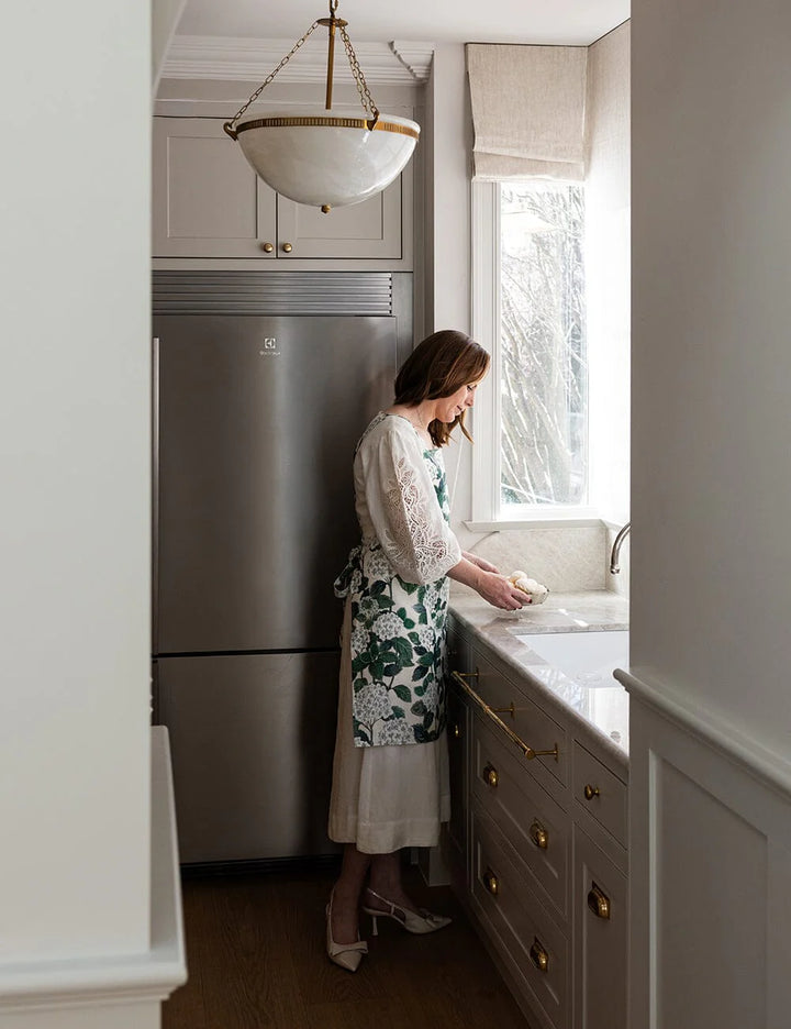 Woman in a kitchen washing dishes in a floral green apron