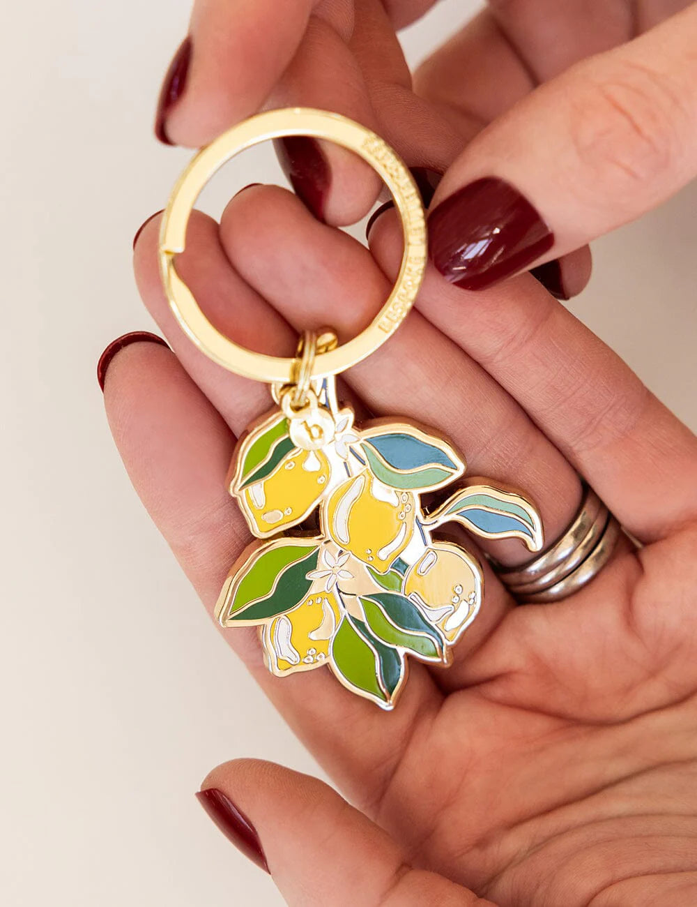 Hand holding a keychain with lemon design on a plain background