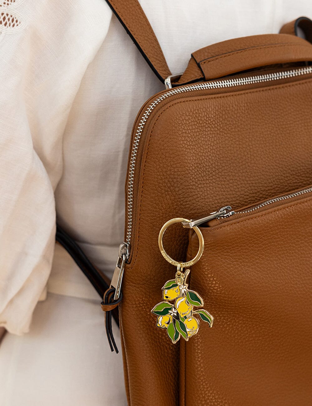 Brown leather bag with a keychain featuring yellow lemons on a light background