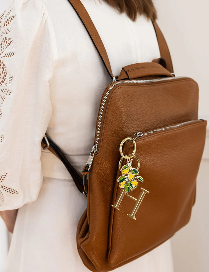 Brown leather backpack with a decorative keychain on a neutral background