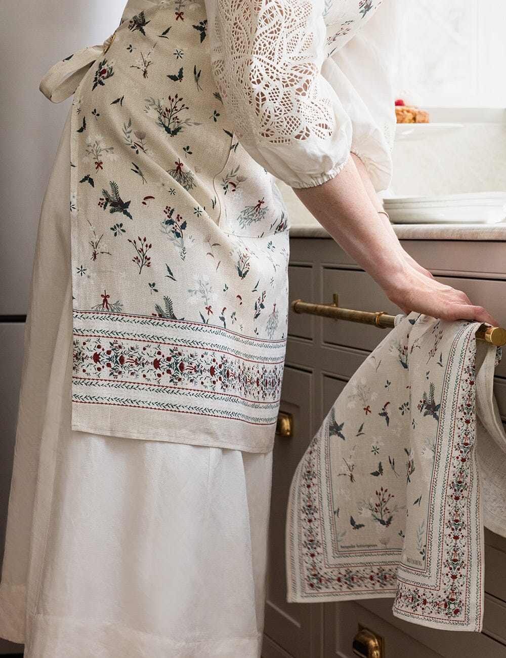 Person wearing a floral apron and holding a matching towel in a kitchen.