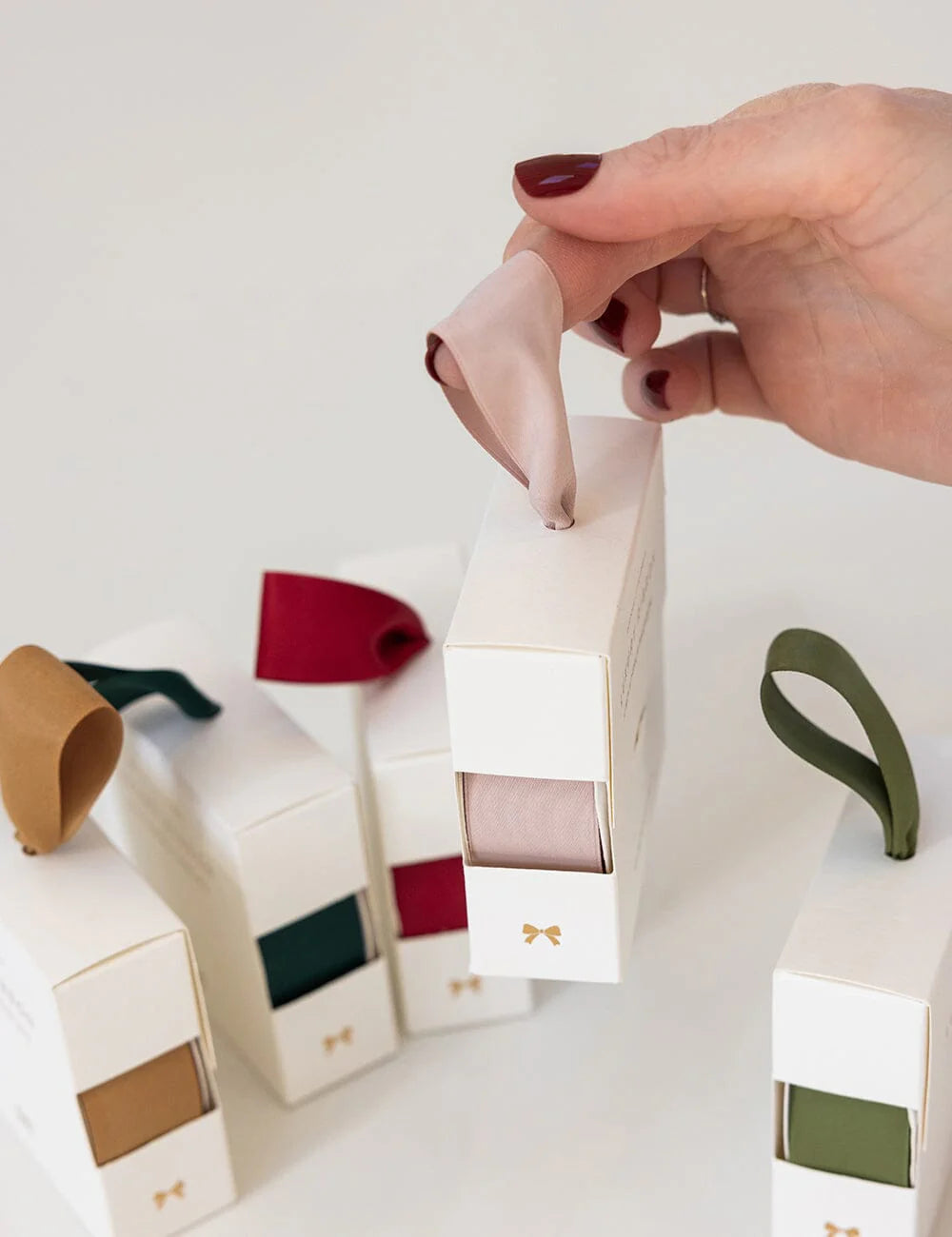 Hand holding nude satin ribbon in white packaging with a different ribbons in the background