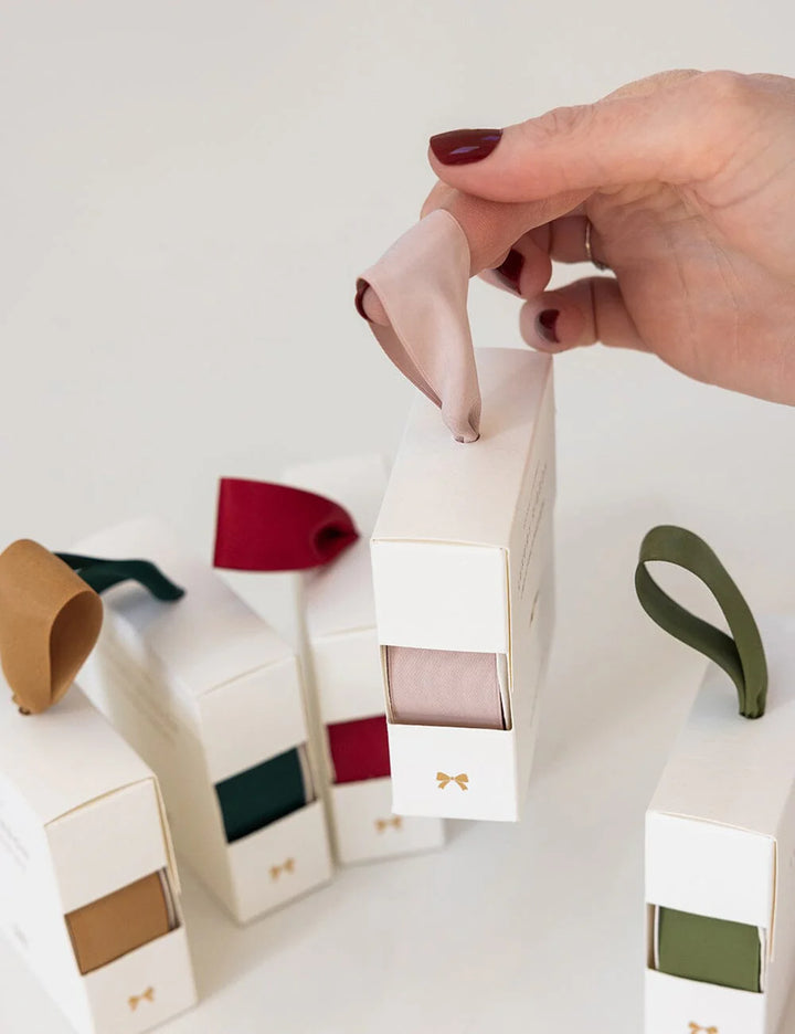 Hand holding nude satin ribbon in white packaging with a different ribbons in the background