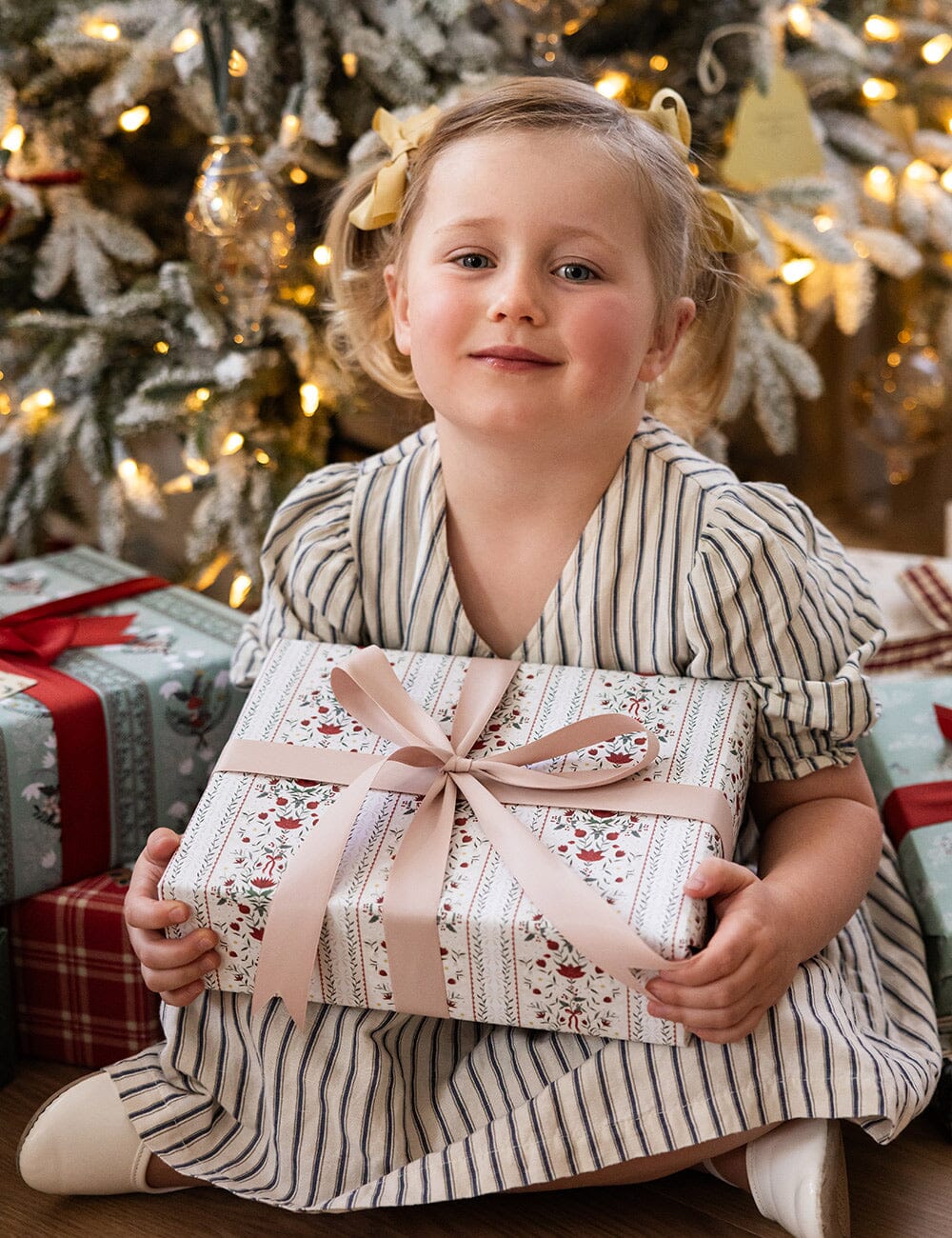 Child holding a wrapped gift in front of a decorated Christmas tree