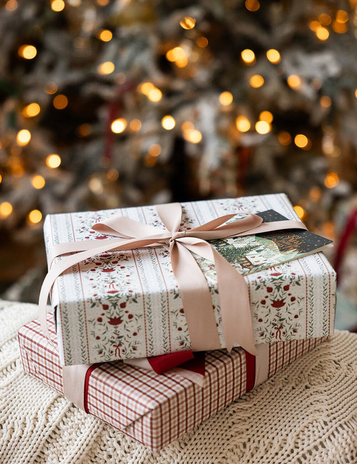 Stack of gift boxes with decorative paper and ribbons in front of a blurred Christmas tree.