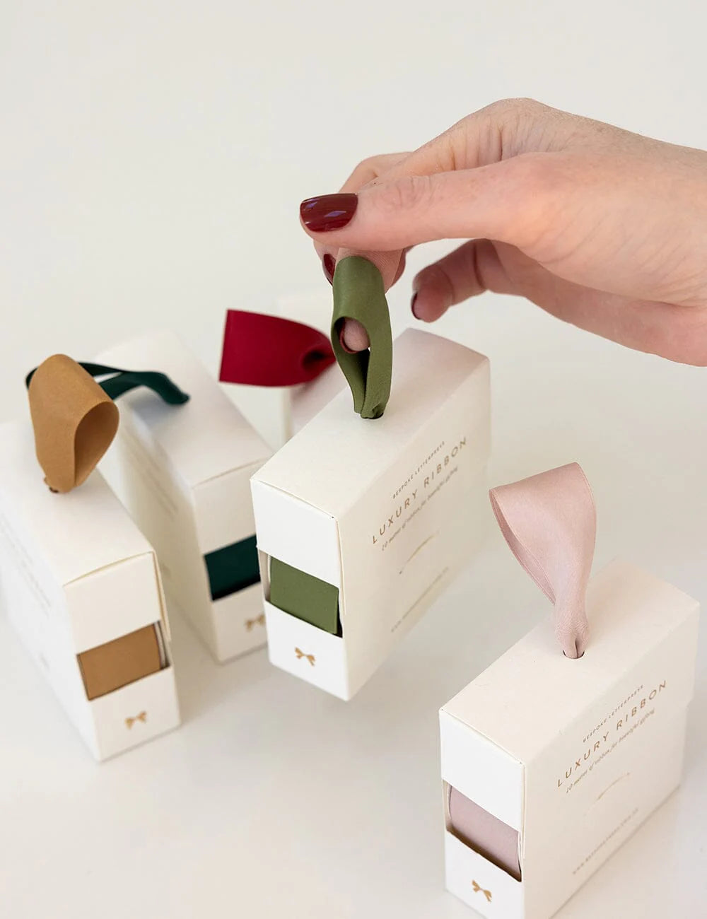 Hand holding a small white box with colorful ribbons on a light background