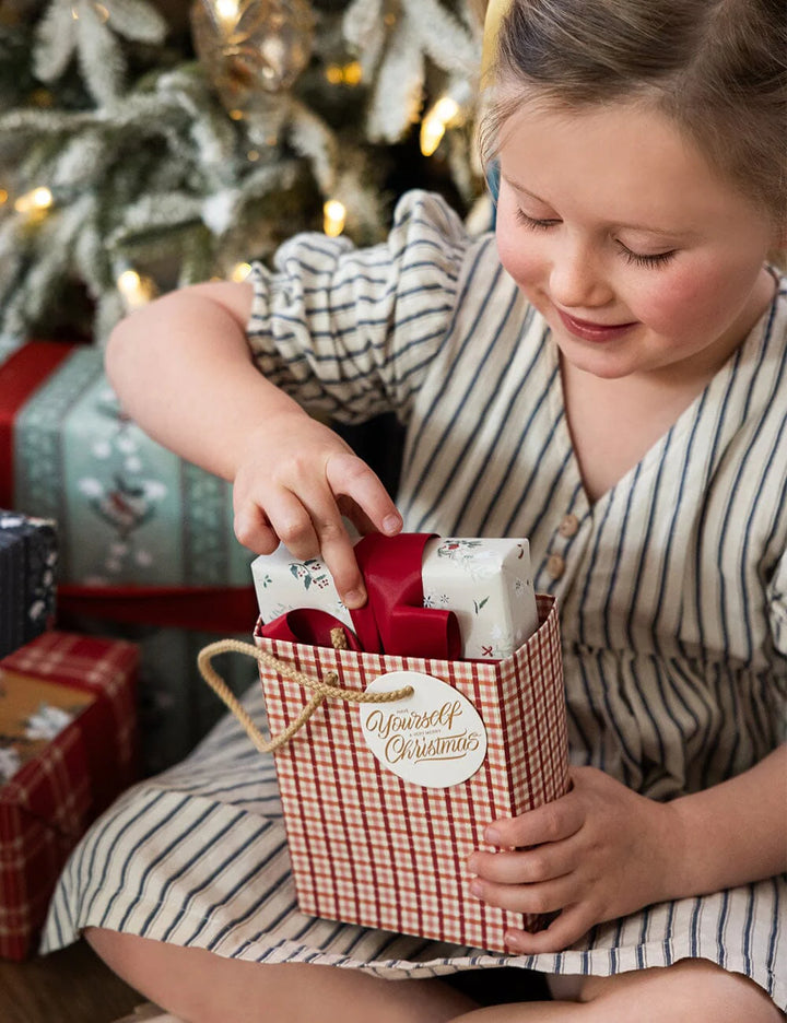Child opening a gift in front of a decorated Christmas tree with presents underneath.