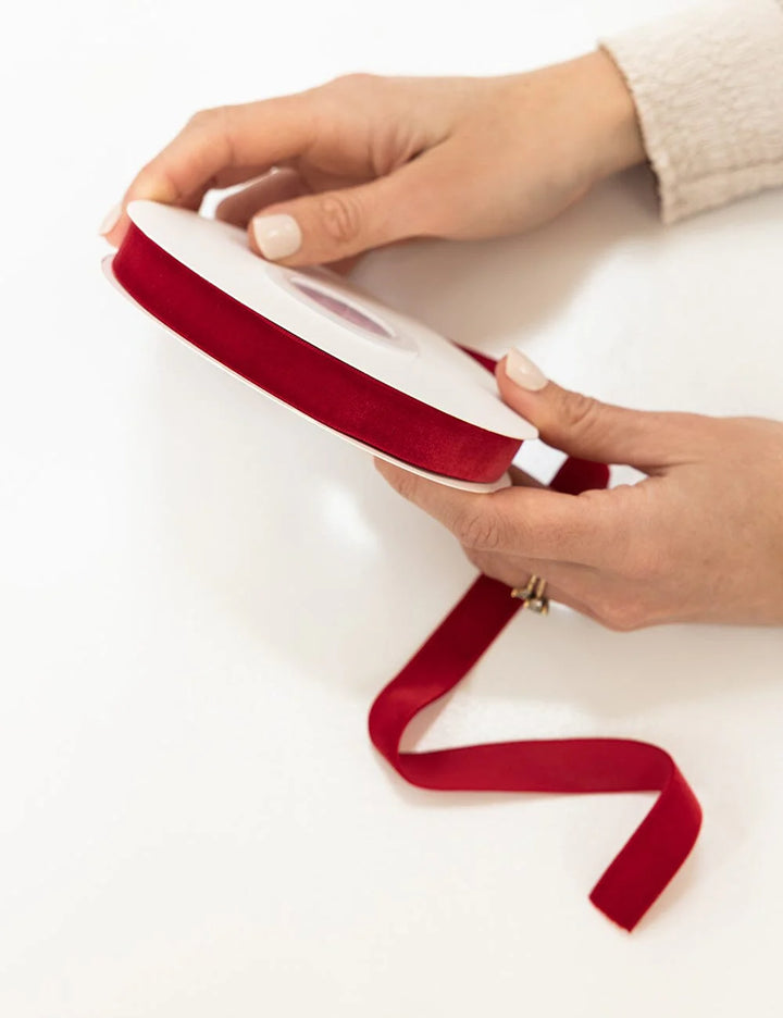 Person holding a roll of red ribbon on a white background