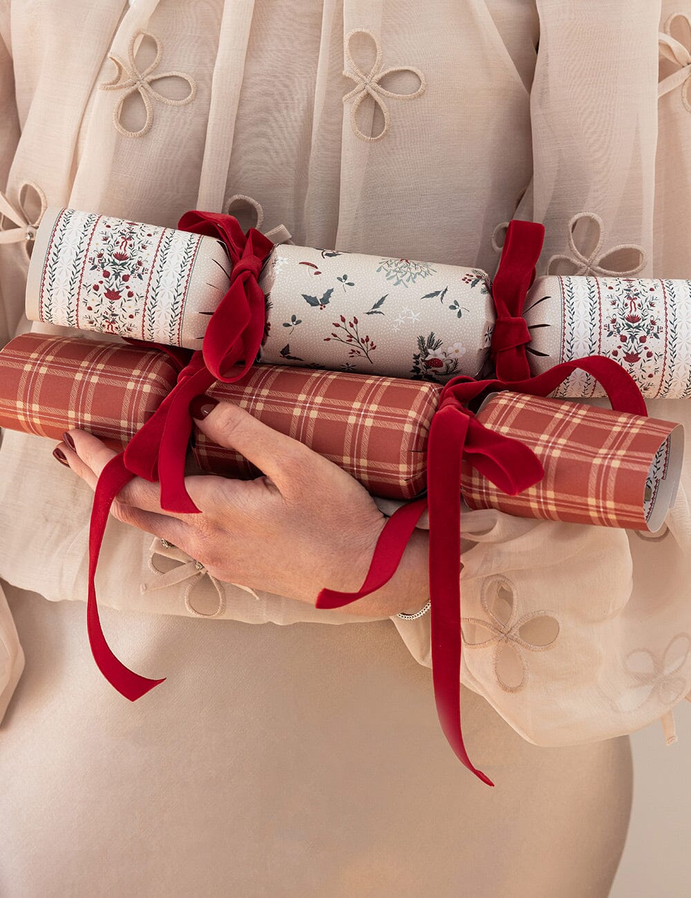 Person holding three rolls of decorative paper with red ribbons against a neutral background