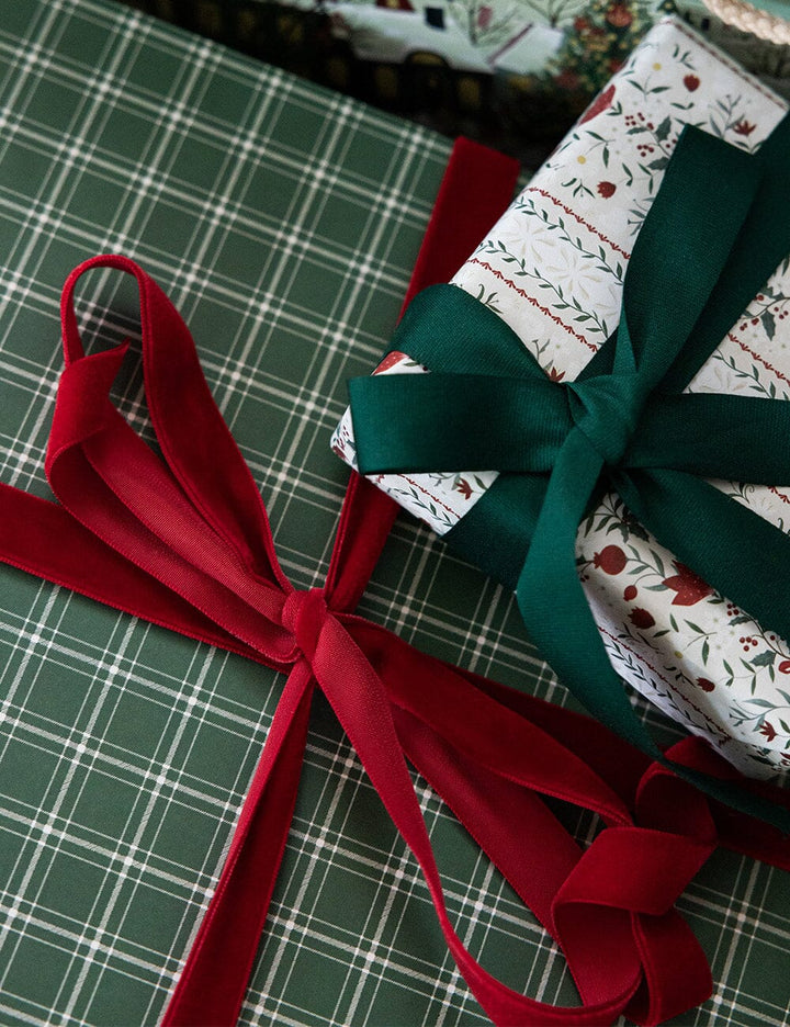 Gift wrapped in green paper with a red ribbon on a plaid surface