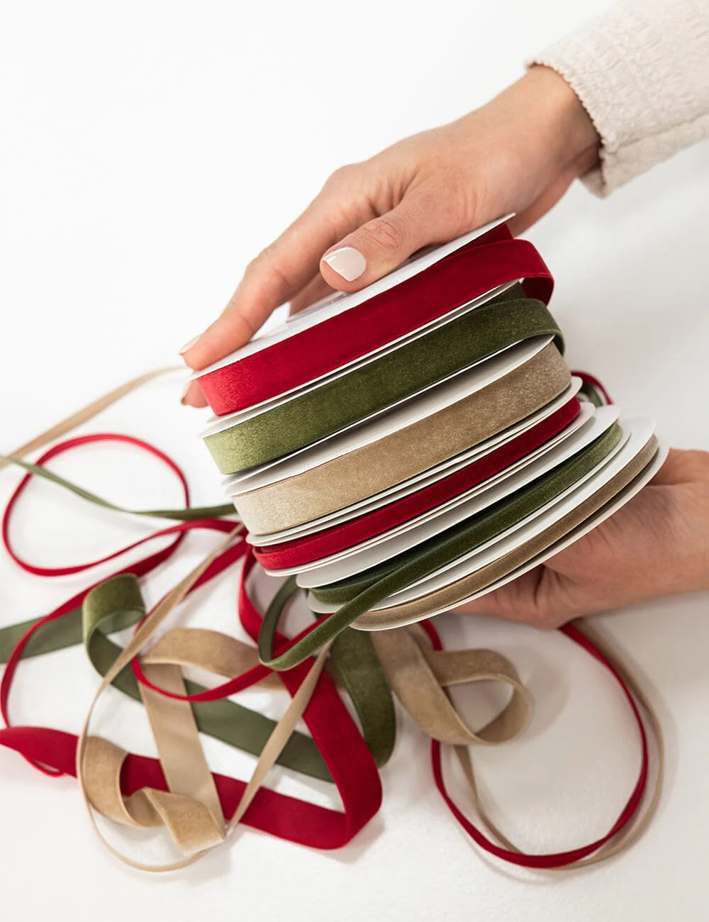 Hand holding a stack of red, green, and beige ribbons on a white background