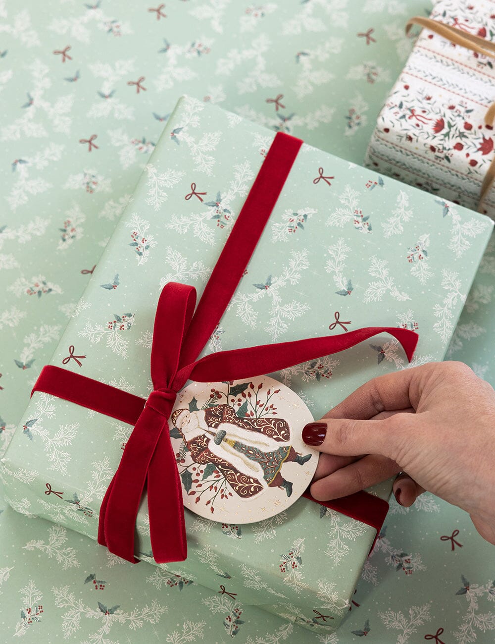 Gift wrapped in green paper with a red ribbon and decorative tag, on a matching patterned surface.