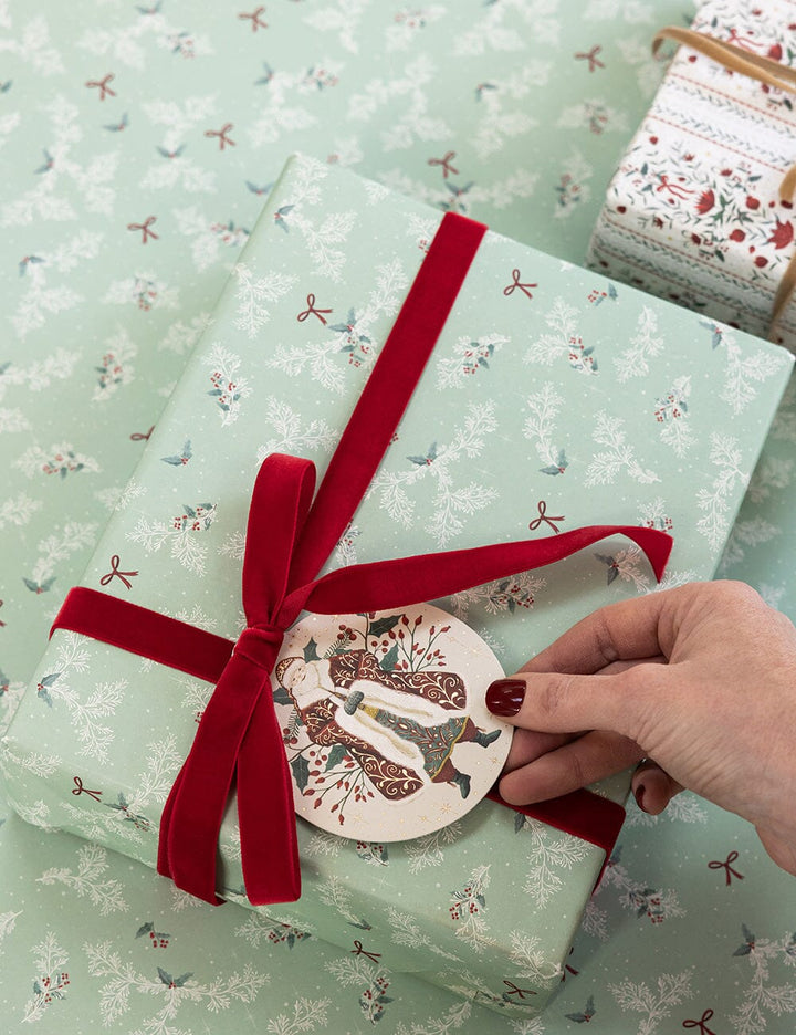 Gift wrapped in green paper with a red ribbon and decorative tag, on a matching patterned surface.