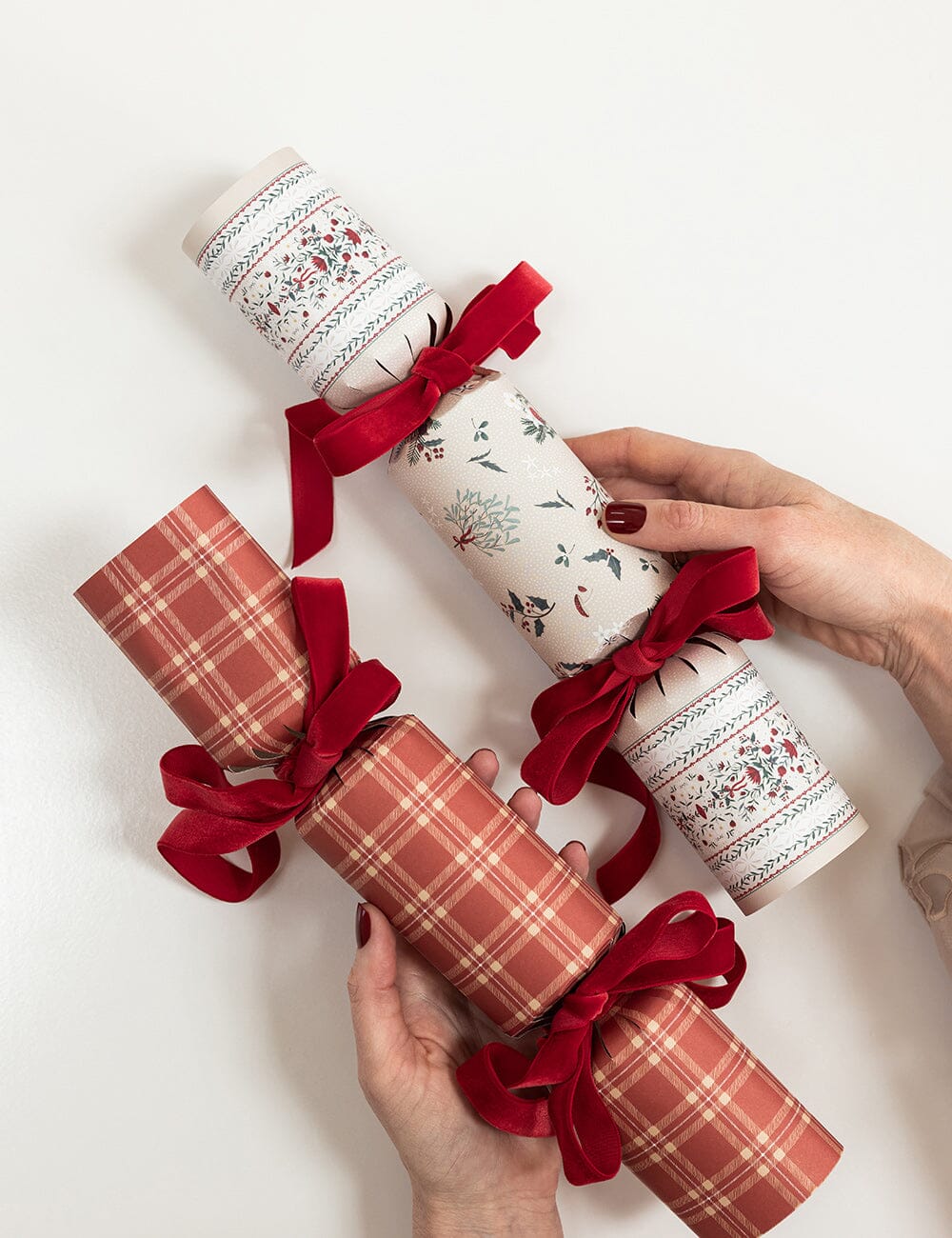 Three Christmas crackers with red ribbons held by hands on a white background
