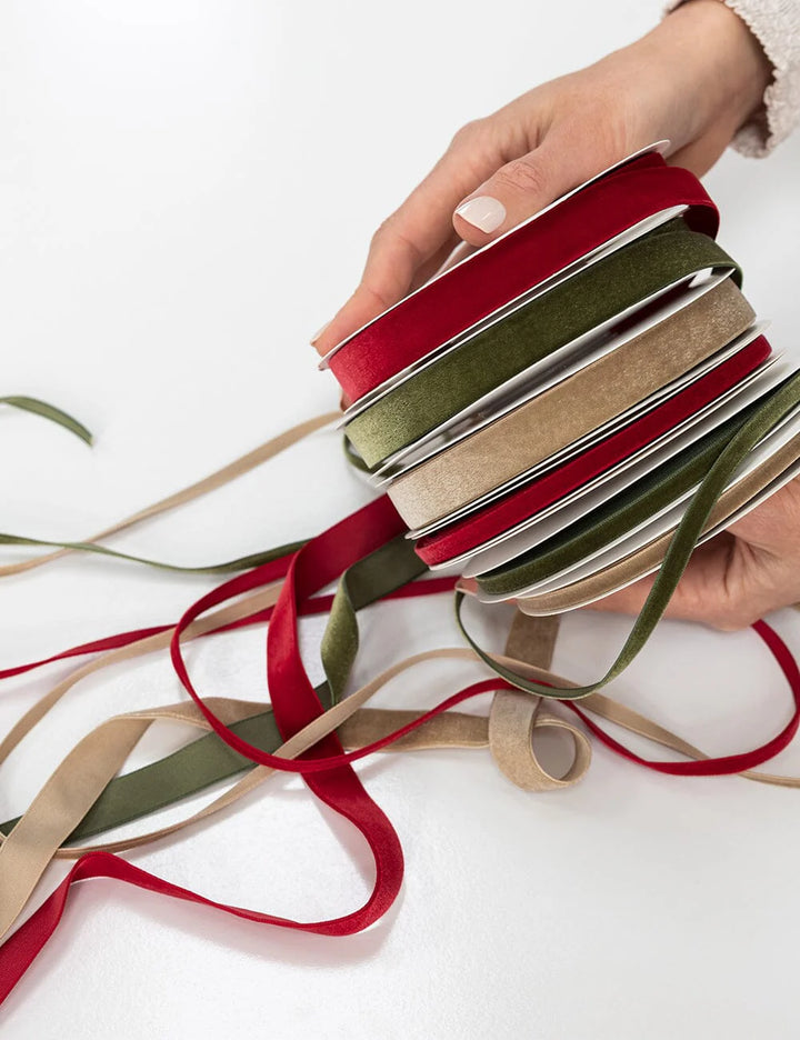 Hand holding a bundle of red, green, and beige ribbons on a white background