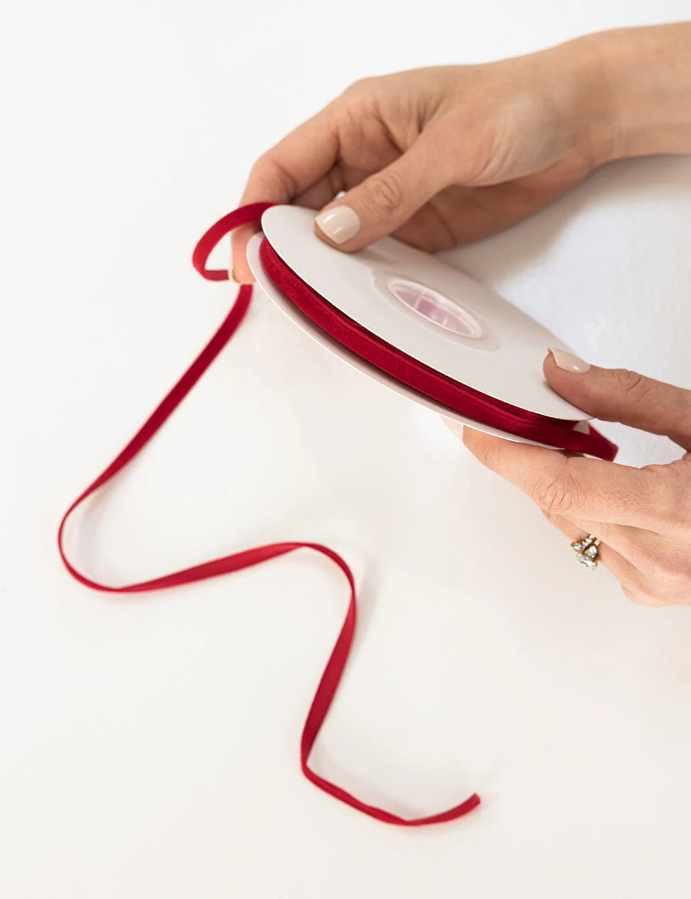 Person holding a red ribbon with a white object on a white background