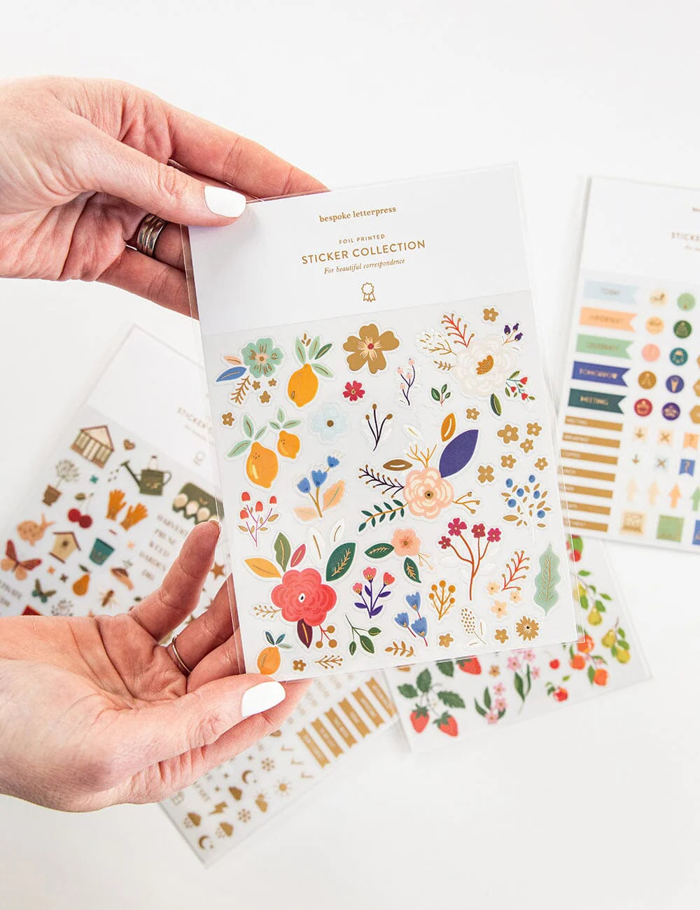 Hand holding a sheet of floral stickers with additional sheets in the background.