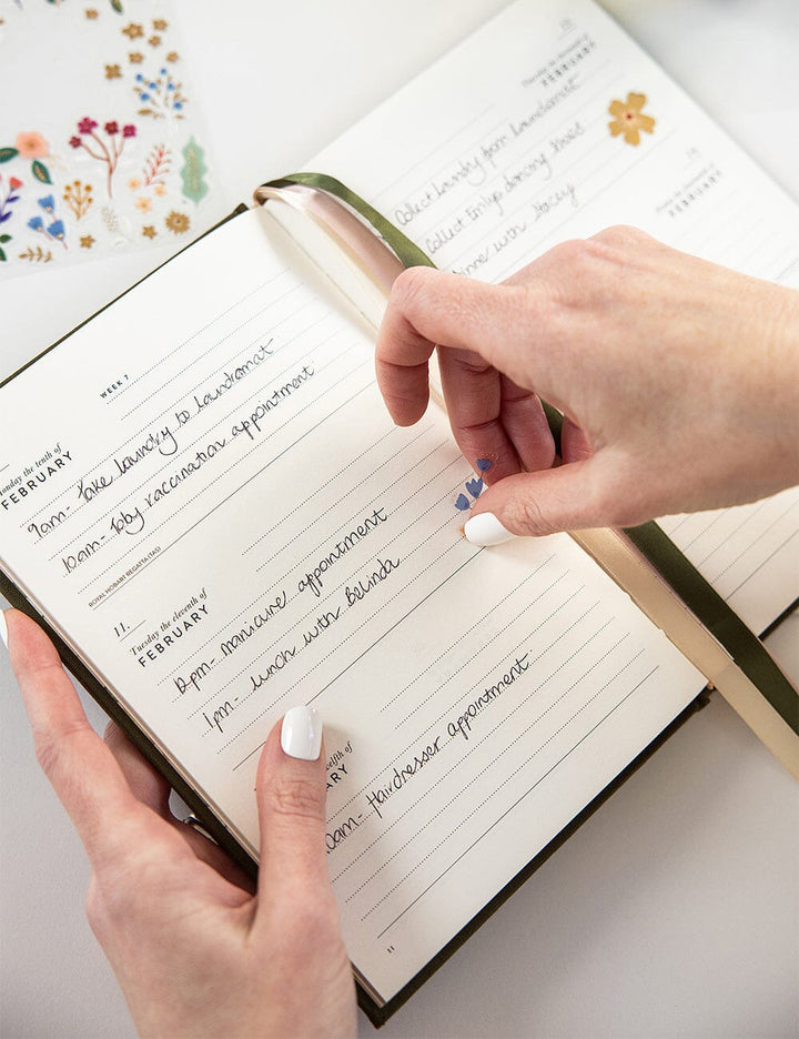 Person writing in a planner with floral designs on a white background