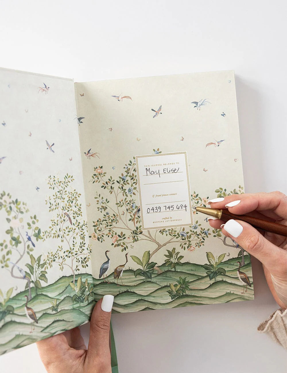 Hand holding a notebook with nature-themed design and contact information