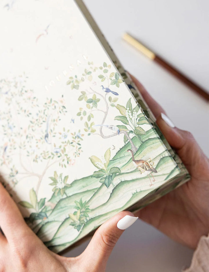 Hand holding a notebook with a nature-themed design on a white background