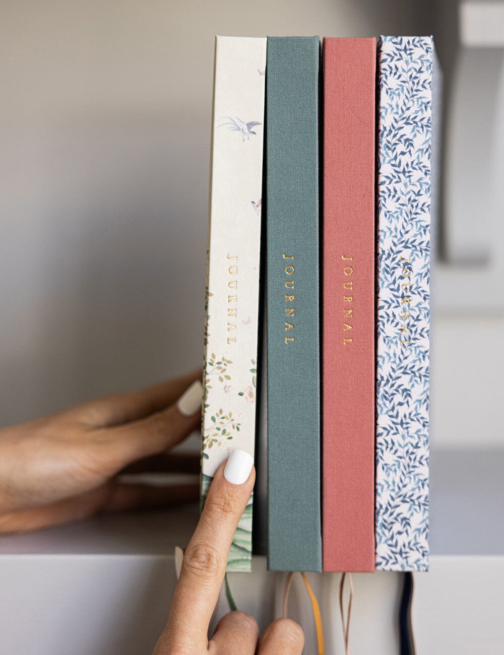 Four patterned notebooks stacked on a shelf with a hand pointing to one of them.
