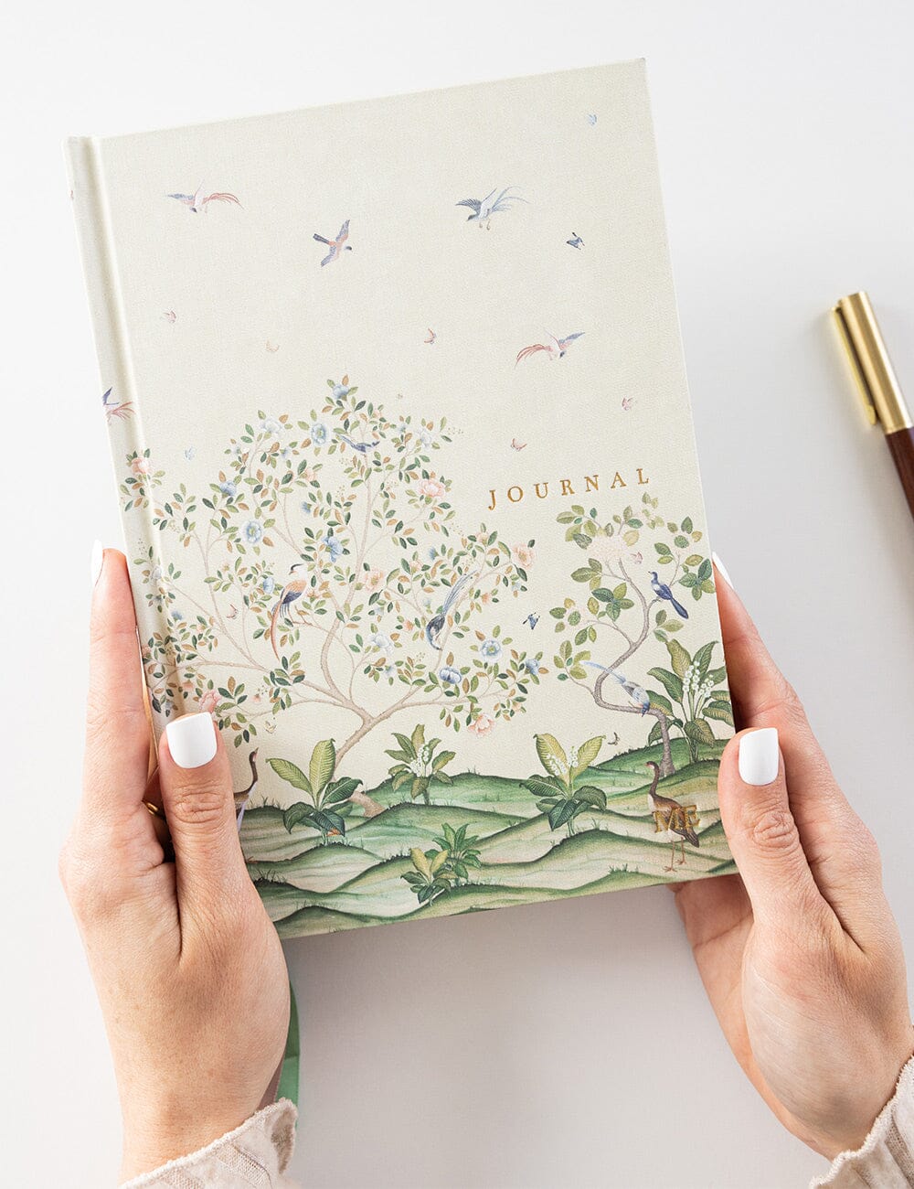 Journal with nature-themed cover held by hands on a light background