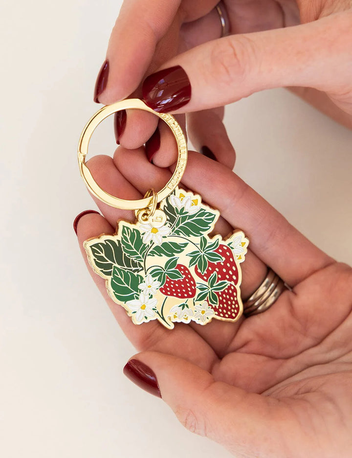 Keychain with strawberry design held by a hand against a white background