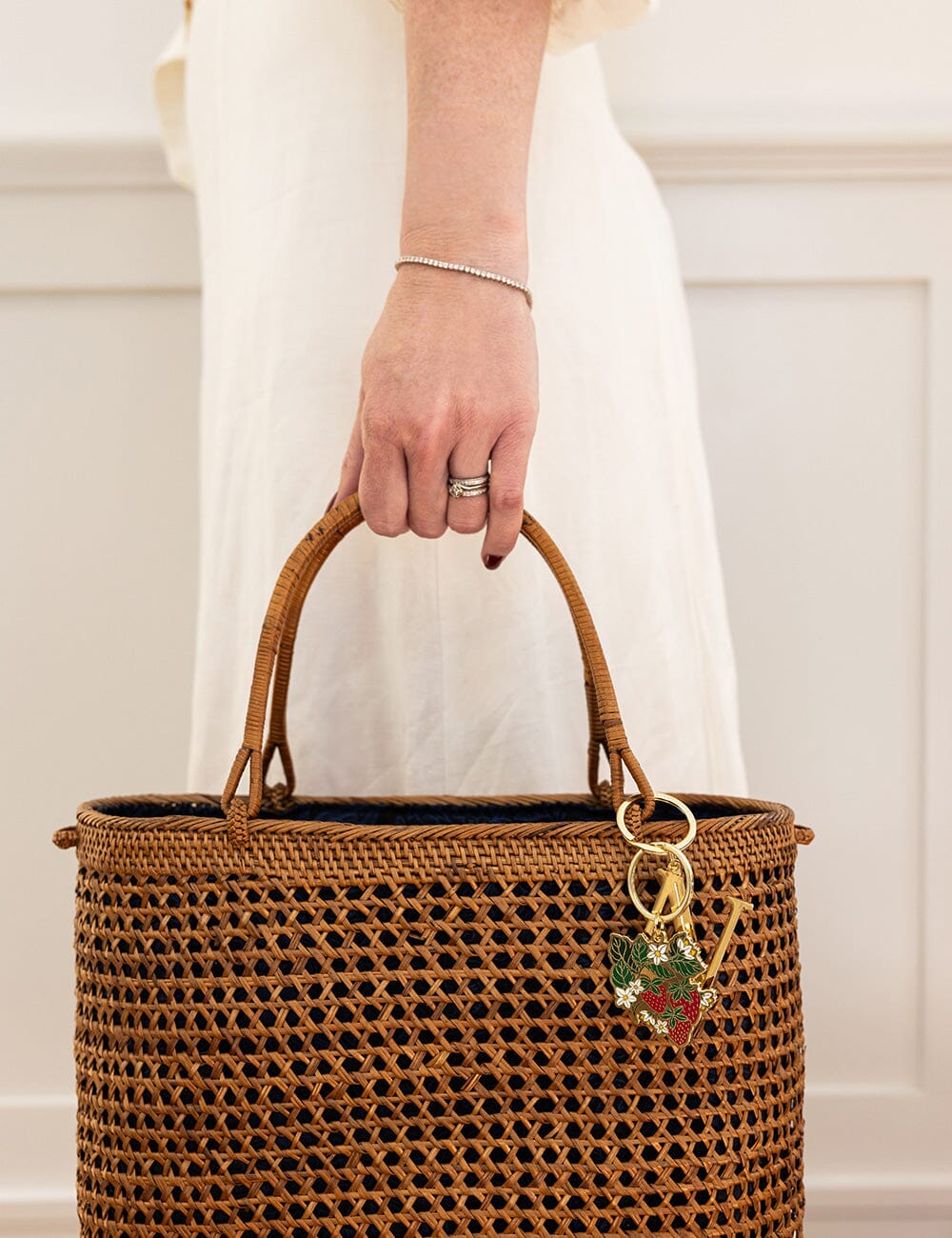Brown woven handbag with a keychain held by a person wearing a white dress.