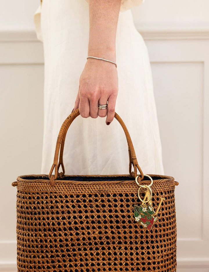 Brown woven handbag with a keychain held by a person wearing a white dress.
