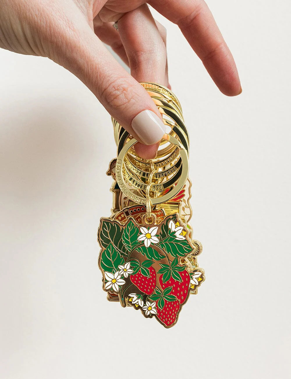 Keychain with strawberry design held by a hand against a white background