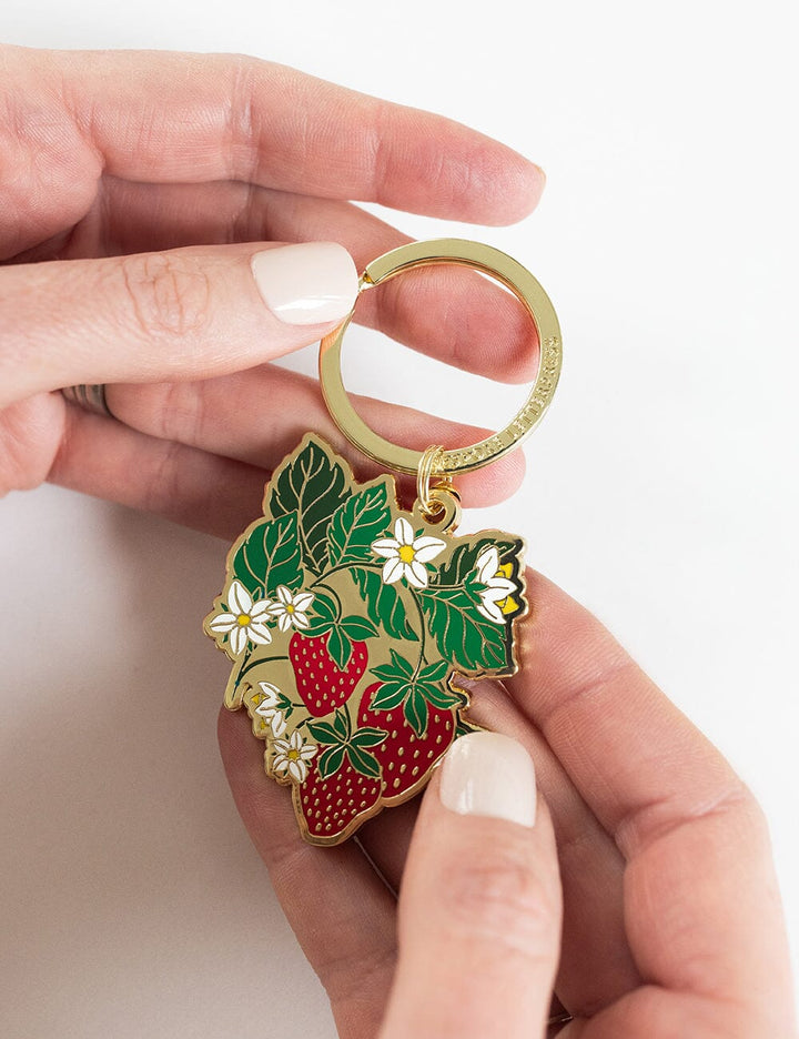 Hand holding a keychain with strawberry design on a white background