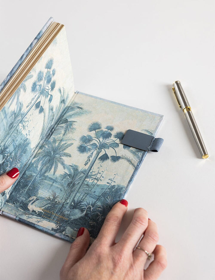 Journal with palm tree design, pen, and hand on a white background
