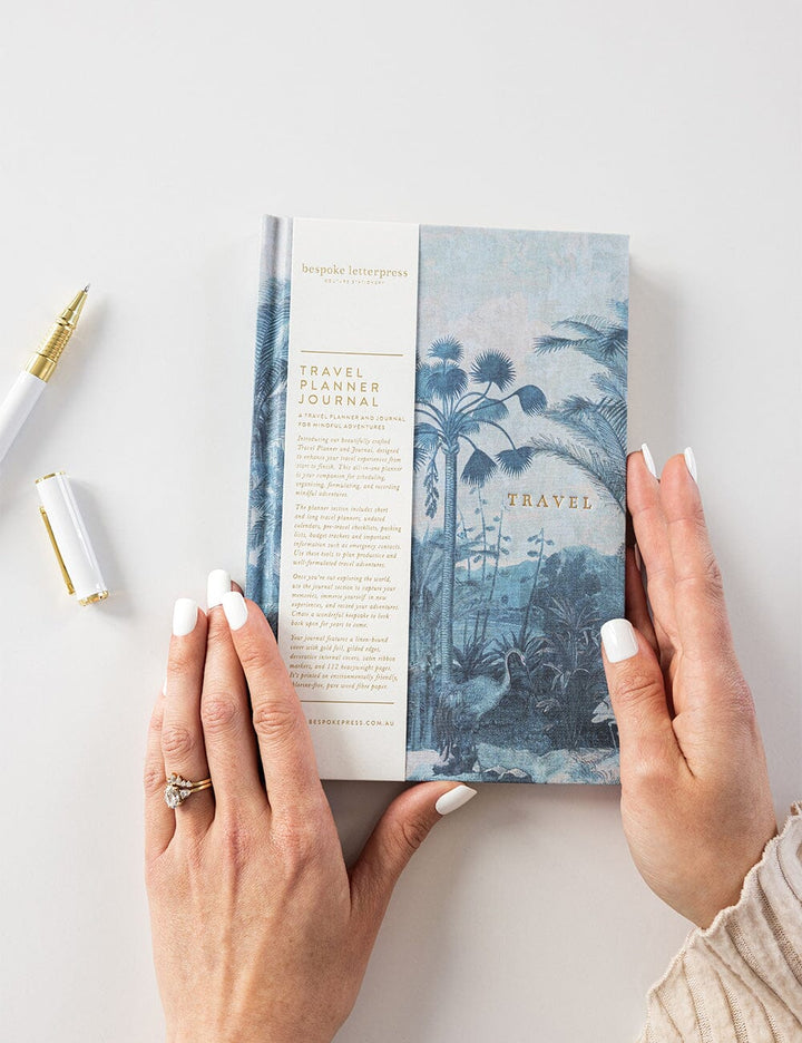 Person holding a travel planner journal with a scenic cover on a light background