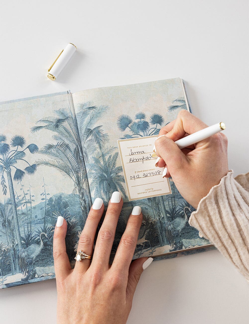 Person writing in a notebook with a scenic cover on a light surface