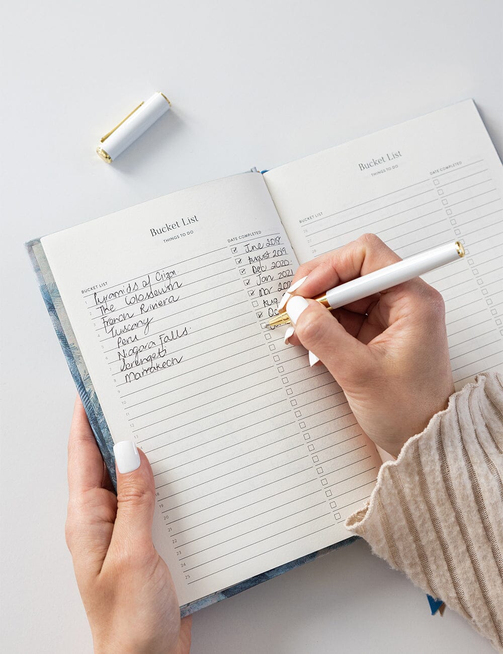 Person writing in a planner with a pen on a light gray background