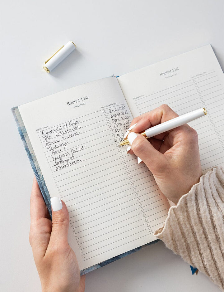 Person writing in a planner with a pen on a light gray background