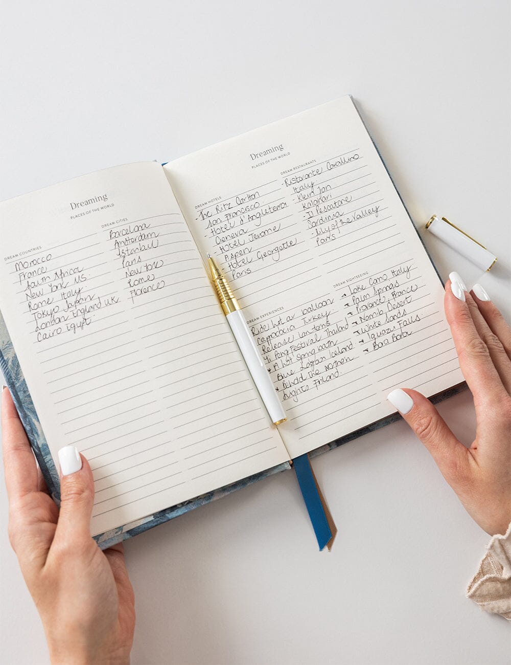 Open notebook with handwritten notes on a white surface, held by two hands.