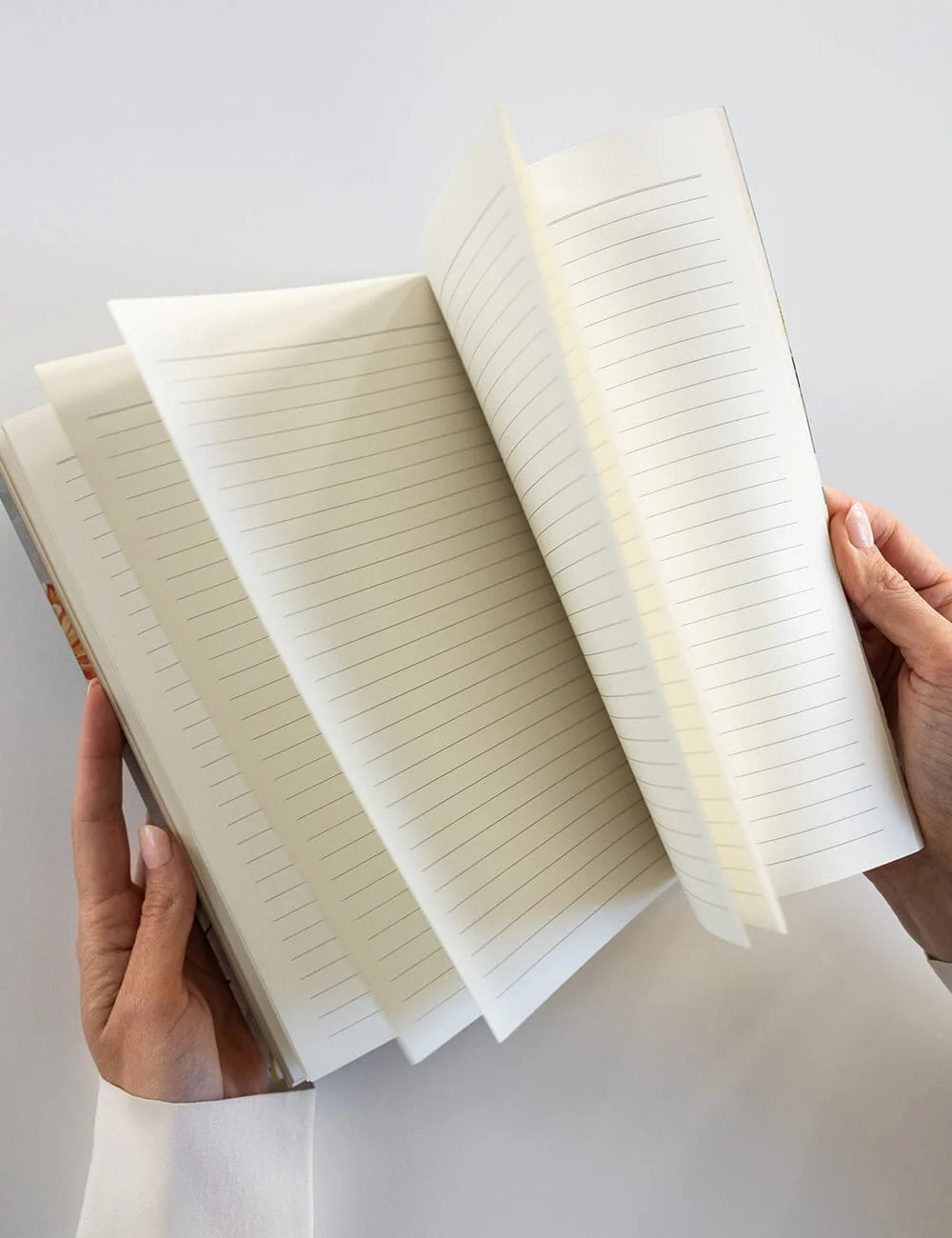 Open notebook held by hands against a light gray background