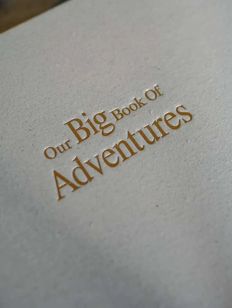 Photo album cover with 'Our Big Book of Adventures' text in gold on a textured beige background